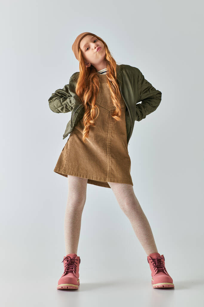 スタイリッシュな冬の衣装とハットパフチークと腰に手で立っている不満の少女 - 写真・画像