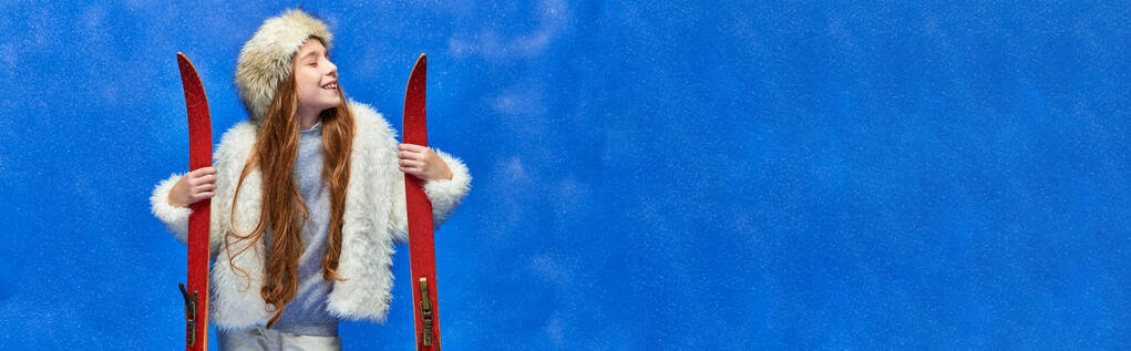 winter vreugde, blij tiener meisje in faux fur jas en hoed met rode ski 's op turquoise, banner - Foto, afbeelding