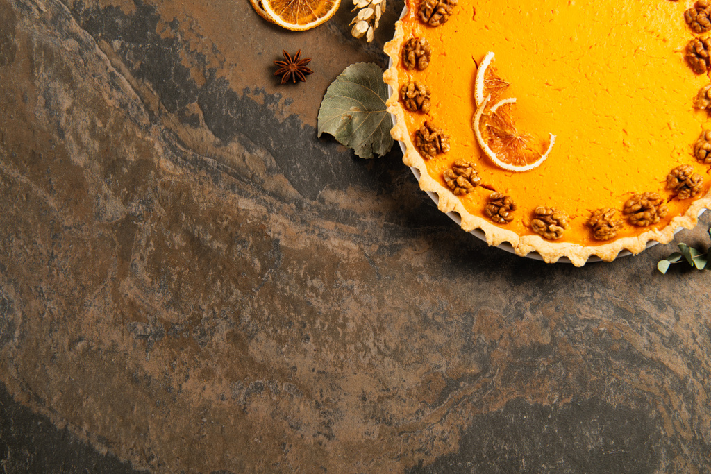 köstlicher Kürbiskuchen mit Orangenscheiben und Walnüssen in der Nähe von Erntedank-Dekor auf rauer Steinoberfläche - Foto, Bild