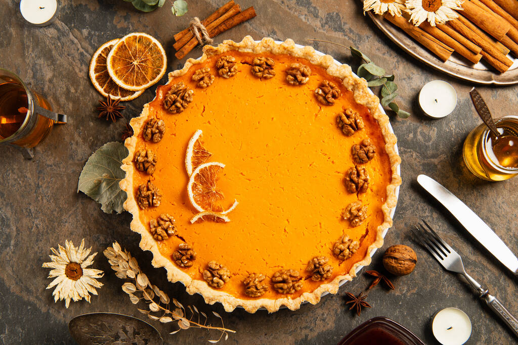 Символы благодарения, тыквенный пирог с грецкими орехами и апельсиновыми ломтиками рядом со специями, травами и теплым чаем - Фото, изображение