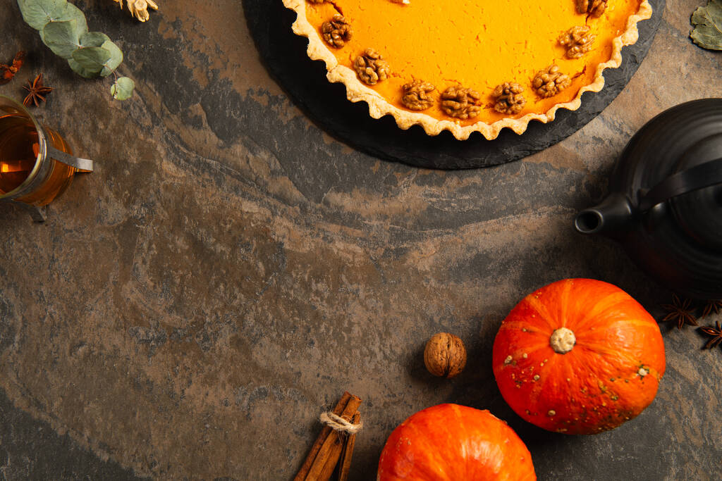 pastel de calabaza de acción de gracias con nueces cerca de calabazas de naranja maduras, especias y té caliente en la mesa de piedra - Foto, Imagen