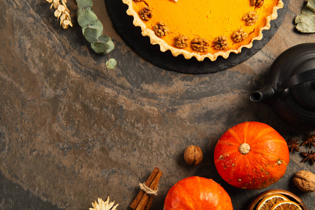 tarte à la citrouille aux noix près de citrouilles mûres, épices et théière sur table en pierre, décor d'action de grâce - Photo, image