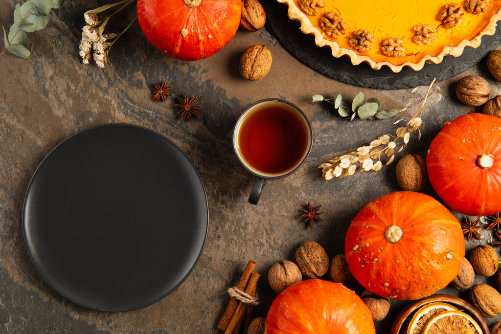 assiette en céramique noire près de citrouilles orange, thé et tarte à la citrouille d'action de grâces sur table en pierre rustique - Photo, image