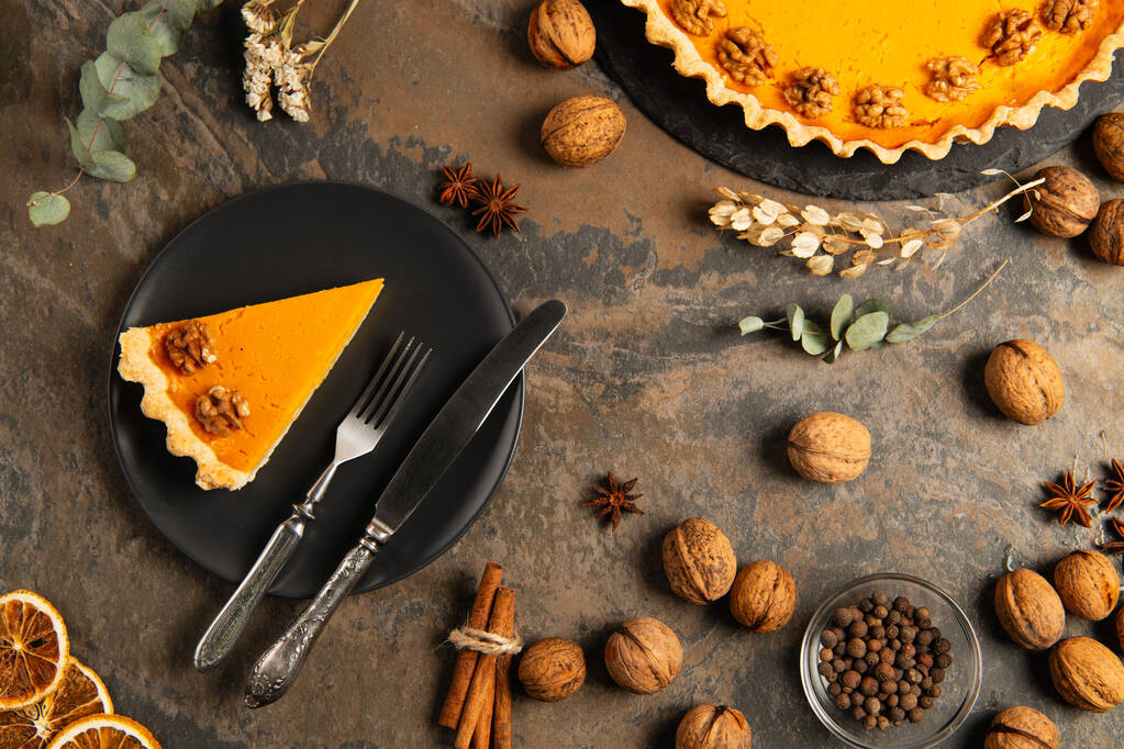 κολοκυθόπιτα ευχαριστιών και μαχαιροπίρουνα σε μαύρο πιάτο κοντά σε πορτοκαλιές κολοκύθες σε διακοσμημένο πέτρινο τραπέζι - Φωτογραφία, εικόνα