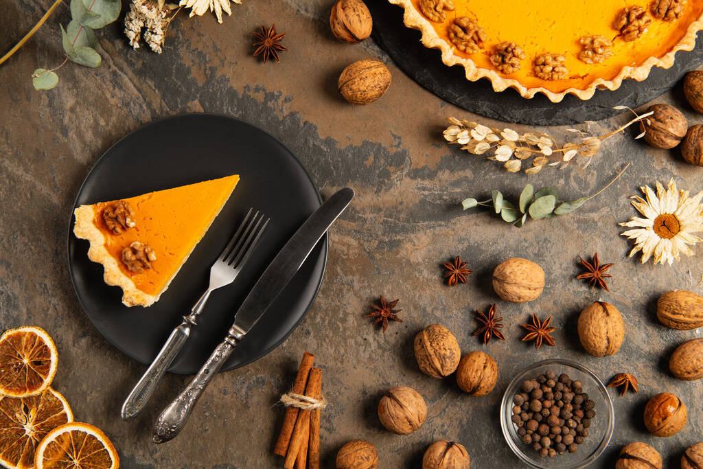 smaczne ciasto dyniowe i sztućce na czarnej ceramicznej płycie w pobliżu pomarańczowych dyni na kamiennym stole, Święto Dziękczynienia - Zdjęcie, obraz