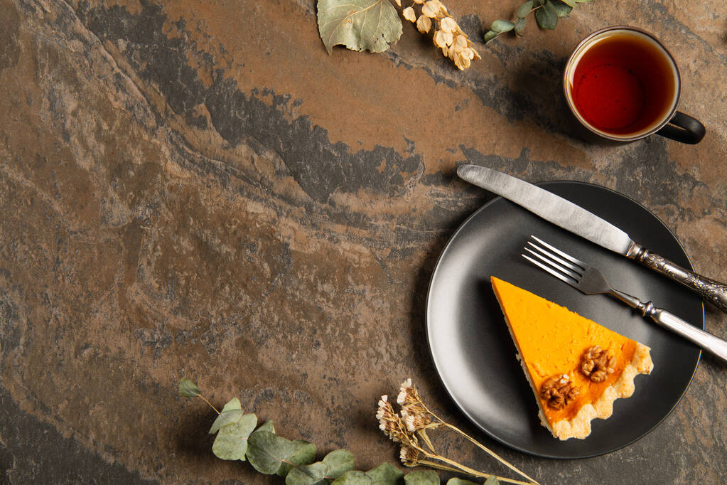 Thanksgiving saisonnier, assiette noire avec tarte à la citrouille près des herbes et thé chaud sur table en pierre - Photo, image