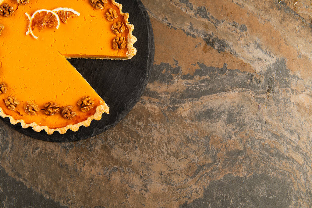 яркий праздничный пирог с грецкими орехами и сушеными оранжевыми ломтиками на черном столе и каменной поверхности - Фото, изображение