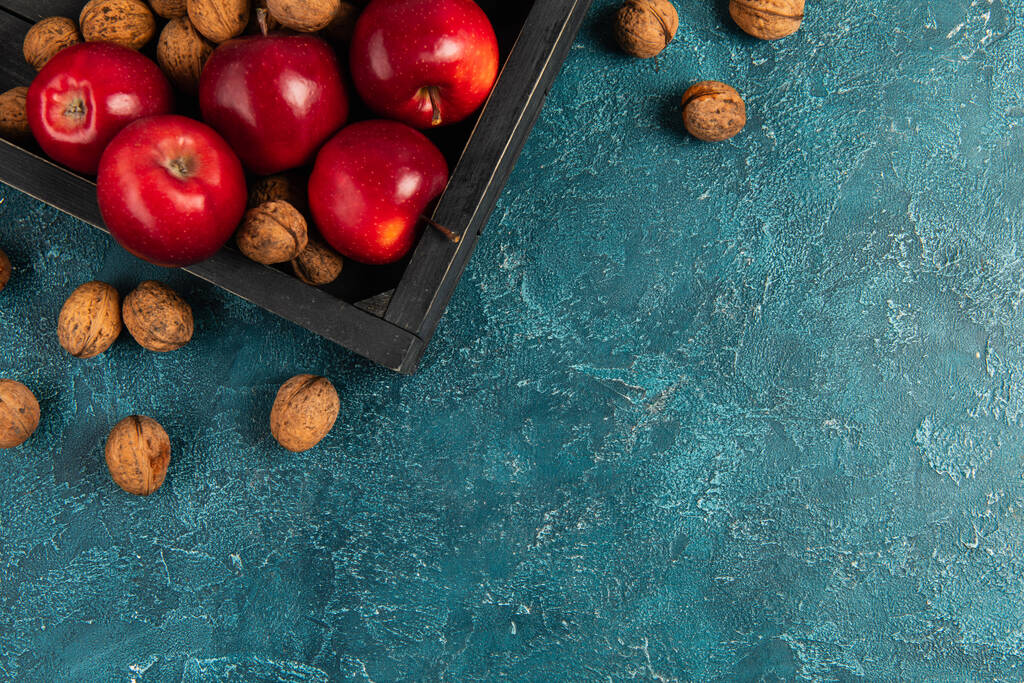 vassoio di legno nero con mele rosse e noci su superficie strutturata blu, impostazione Ringraziamento - Foto, immagini