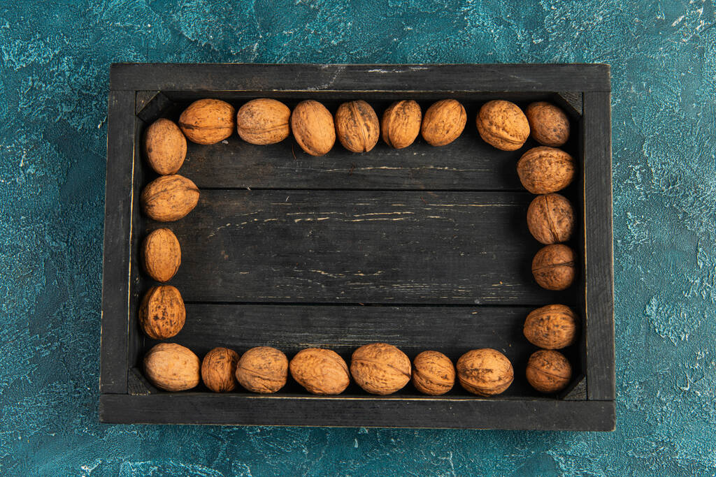 autumnal backdrop with walnuts in black wooden tray on blue textured surface, thanksgiving concept - Photo, Image