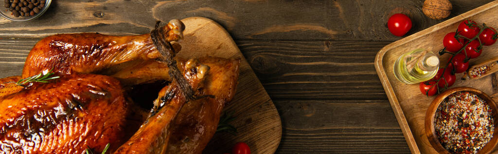 γεύμα Ευχαριστιών, ψητή γαλοπούλα κοντά σε κόκκινα ντοματίνια και μπαχαρικά σε ρουστίκ ξύλινο τραπέζι, πανό - Φωτογραφία, εικόνα