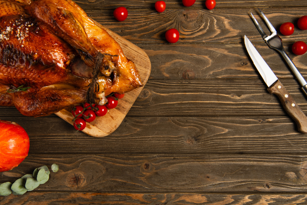 délicieux thanksgiving, dinde rôtie et tomates cerises près des couverts sur table en bois texturé - Photo, image