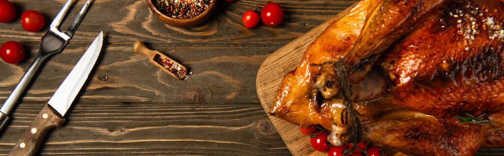 ψητή γαλοπούλα Ευχαριστιών κοντά σε μπαχαρικά, μαχαιροπήρουνα και κόκκινα ντοματίνια σε ξύλινο τραπέζι, λάβαρο - Φωτογραφία, εικόνα