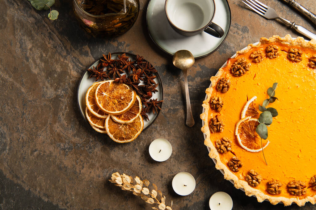 kiitospäivän teema, koristeltu kurpitsapiirakka lähellä kynttilöitä ja appelsiininviipaleita mausteilla kivipöydällä - Valokuva, kuva