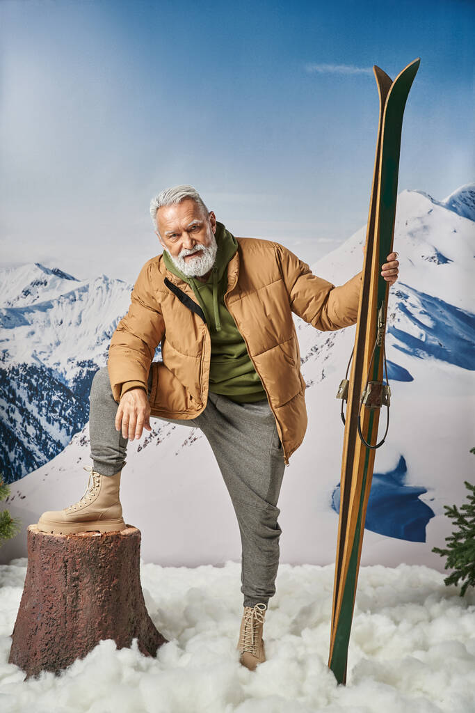 スポーティな服装でサンタとして服を着たジョリーマンは,スキー,クリスマスのコンセプトを保持する木スタンプに彼の足を置きます - 写真・画像