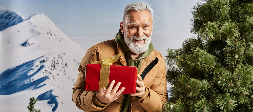 vrolijk kerstman houden aanwezig en glimlachen op de camera met bergen achtergrond, winter concept, banner - Foto, afbeelding