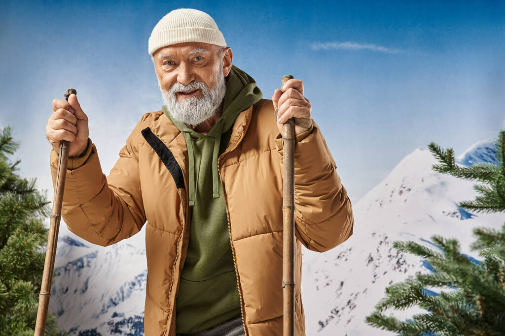 homme joyeux debout sur des skis portant chapeau blanc et veste avec toile de fond de montagnes, concept d'hiver - Photo, image