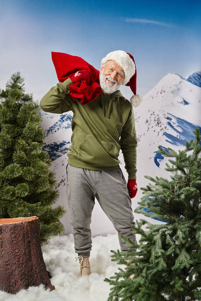 atletische Kerstman in warme kerstmis hoed en wanten met rode grote huidige zak, winter concept - Foto, afbeelding
