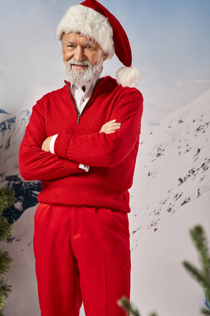 veselý bílý vousatý muž oblečený v kostýmu Santa křížení ruce s úsměvem na kameru, zimní koncept - Fotografie, Obrázek