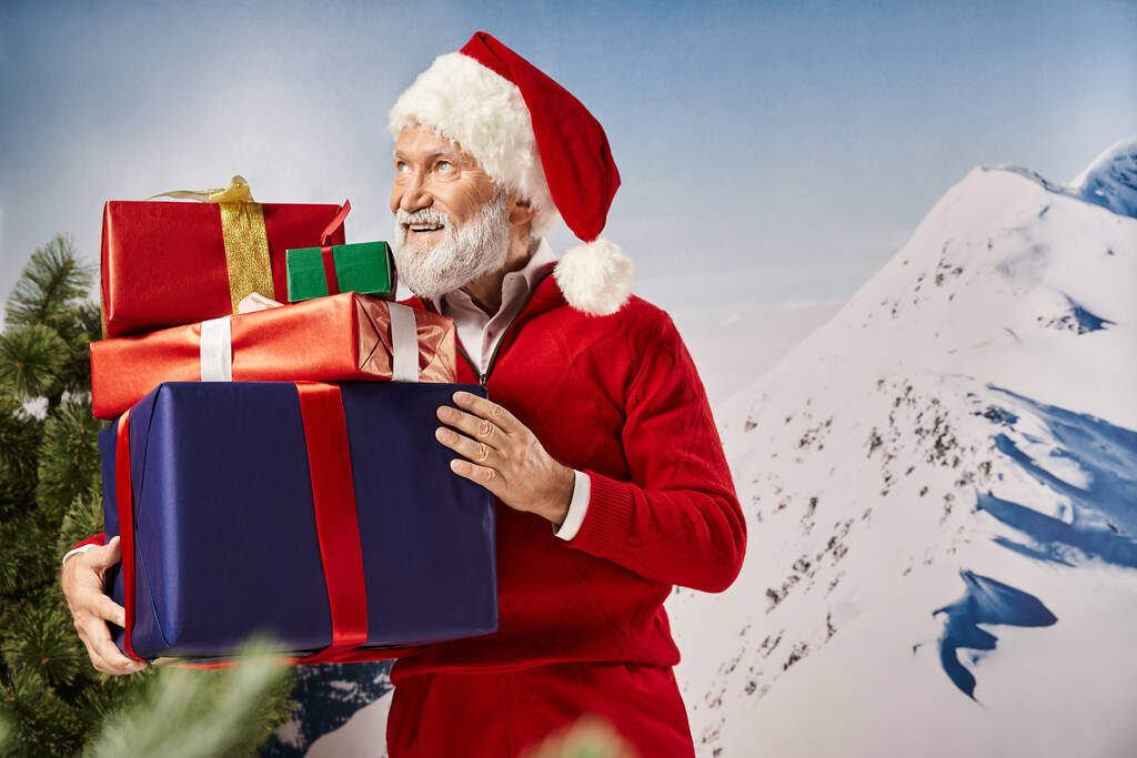 hombre guapo en traje de Santa con regalos en las manos sonriendo y mirando hacia otro lado, concepto de invierno - Foto, Imagen