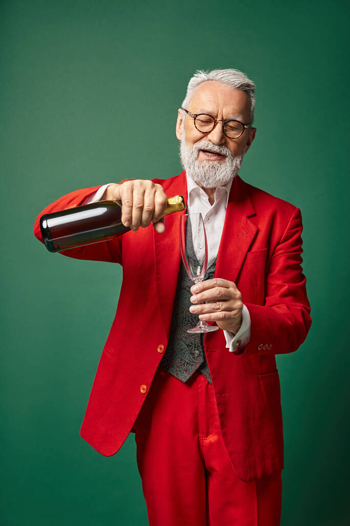 fröhlicher Weihnachtsmann mit weißem Bart gießt Flötenglas mit Champagner auf grünem Hintergrund, Winterkonzept - Foto, Bild