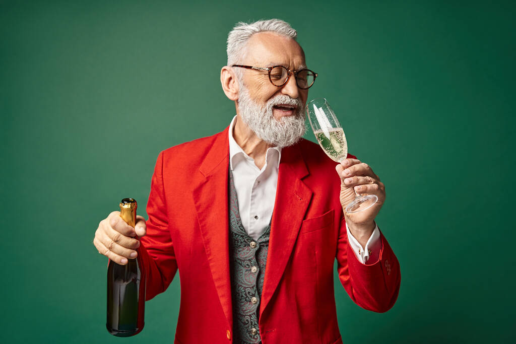 classy jolly Santa Claus enjoying champagne and smiling on dark green backdrop, winter concept - Photo, Image