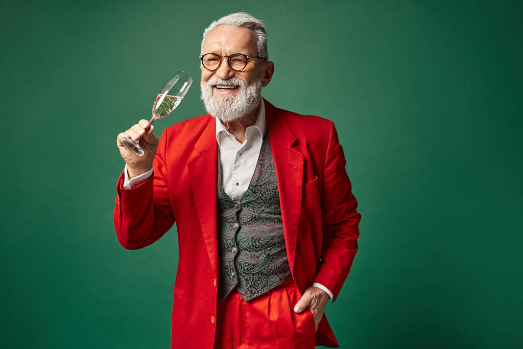 uomo allegro vestito da Babbo Natale godendo bicchiere di champagne con una mano in tasca, concetto invernale - Foto, immagini