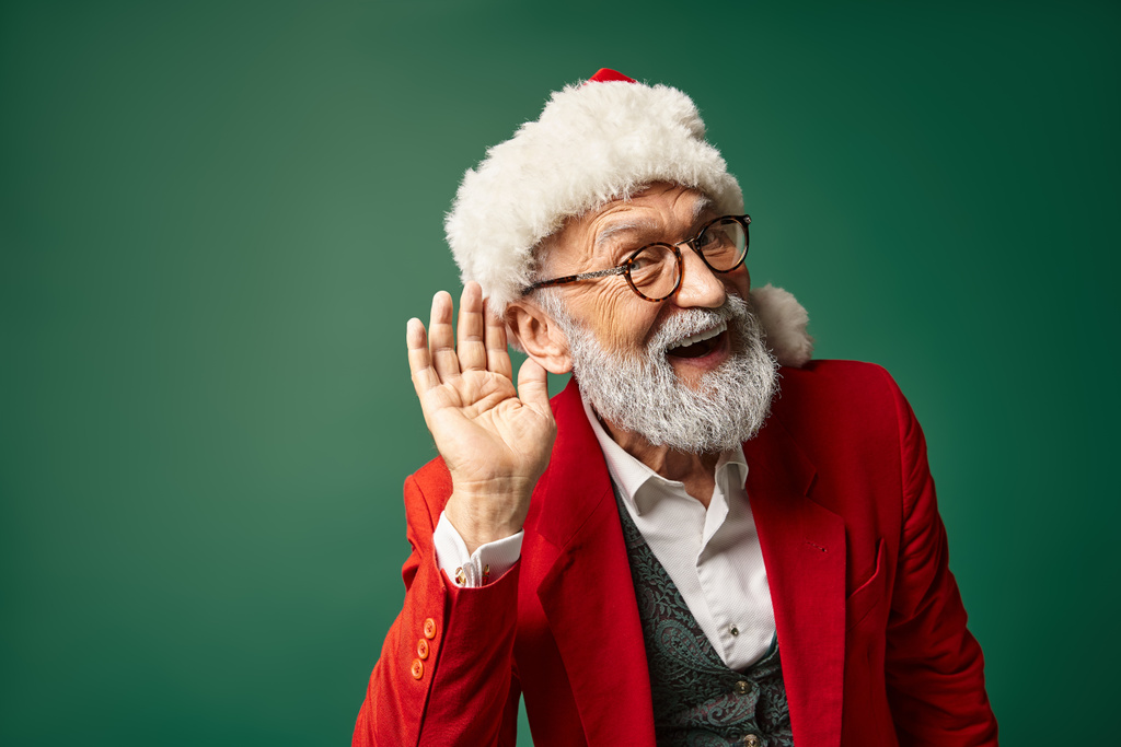 homem alegre vestido como Papai Noel com chapéu vermelho com mão perto da orelha olhando para a câmera, conceito de inverno - Foto, Imagem