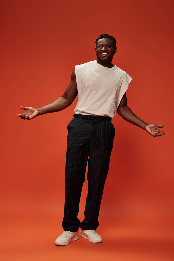 щасливий афроамериканський чоловік у модному повсякденному одязі, що показує вітальний жест з відкритими руками на червоному - Фото, зображення