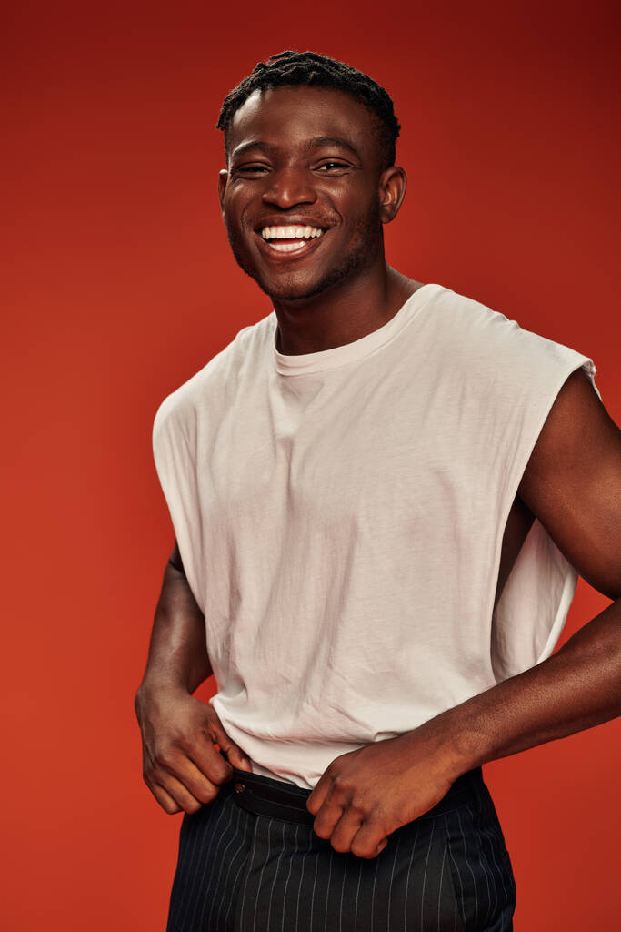 vrolijk Afrikaans amerikaans guy in trendy casual kleding kijken naar camera en lachen op rood - Foto, afbeelding