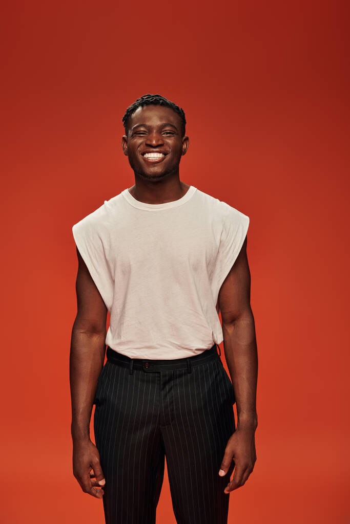 vista frontal del hombre afroamericano complacido en ropa casual elegante sonriendo a la cámara en rojo - Foto, imagen