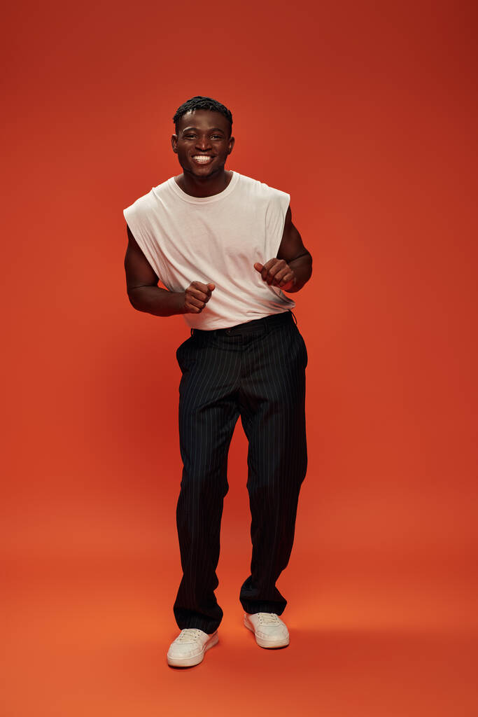 overjoyed african american man in fashionable casual clothes posing on red and orange backdrop - Photo, Image