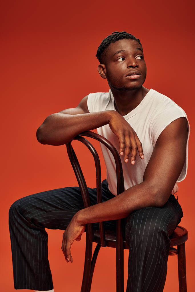 zamyślony i stylowy Afrykański Amerykanin w białej koszuli zbiornika siedzi na krześle i patrzy w czerwień - Zdjęcie, obraz