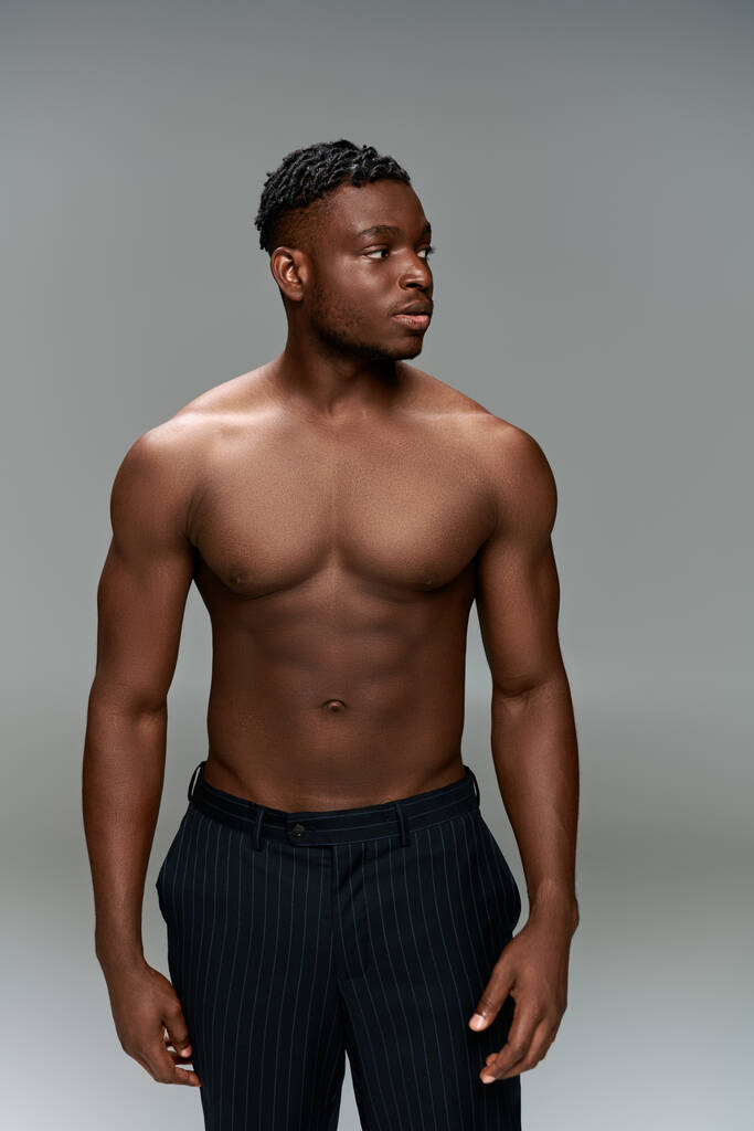 bez košile africký Američan s svalnatým tělem pózuje v černých kalhotách a dívá se jinam na šedé - Fotografie, Obrázek