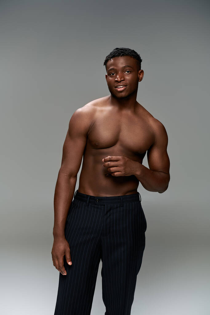 позитивная африканская модель фитнеса с туловищем без рубашки, смотрящая на камеру на сером фоне - Фото, изображение