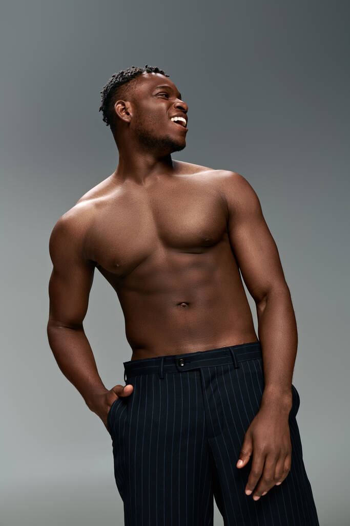 Веселый африканский американец с мускулистым телом и рукой в кармане, смотрящий в сторону на серого - Фото, изображение