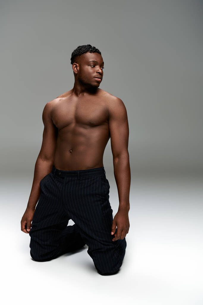 sportivo uomo africano americano in pantaloni neri con forte corpo senza maglietta in posa sulle ginocchia su grigio - Foto, immagini