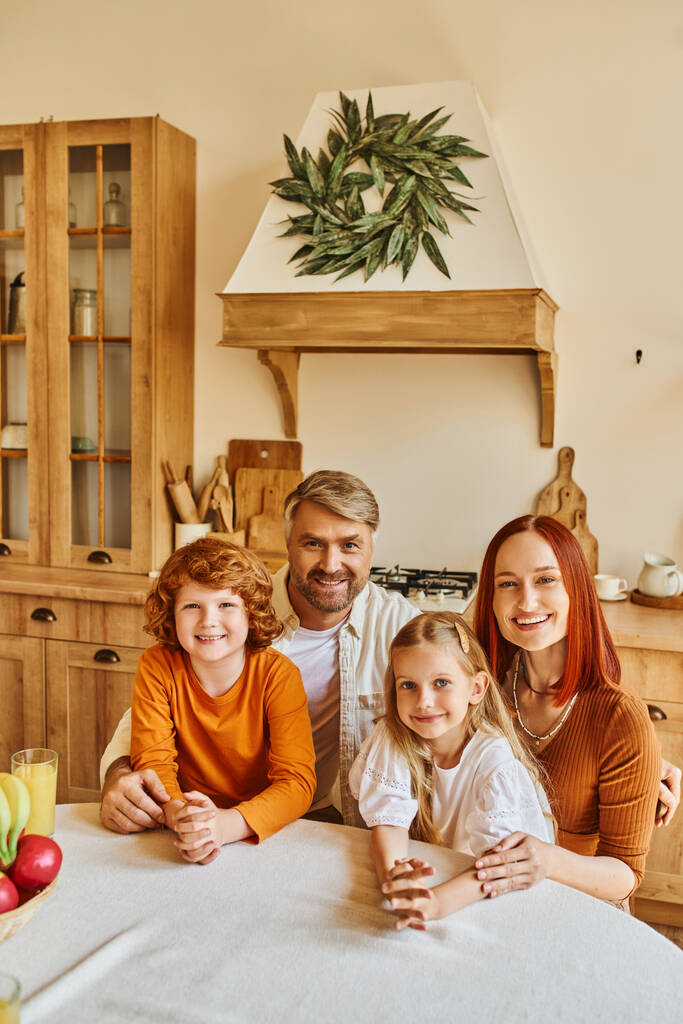 uśmiechnięci rodzice z synem i córką patrzący przed kamerą w kuchni, szczęśliwy rodzinny portret w domu - Zdjęcie, obraz