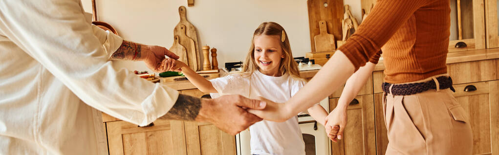 radosna dziewczyna trzymająca się za ręce i bawiąca się z rodzicami w przytulnej kuchni, zabawy i śmiechu, sztandar - Zdjęcie, obraz