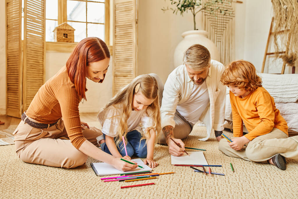 freudige Eltern und Kinder, die gemeinsam auf dem Fußboden im modernen Wohnzimmer zeichnen und Kreativität ausdrücken - Foto, Bild