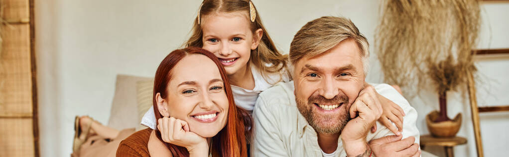 joyful parents with carefree daughter relaxing in bedroom and looking at camera, horizontal banner - Photo, Image