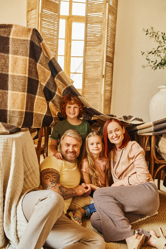 padres y niños emocionados sentados debajo de una choza de mantas en la sala de estar, jugando juntos en casa - Foto, imagen