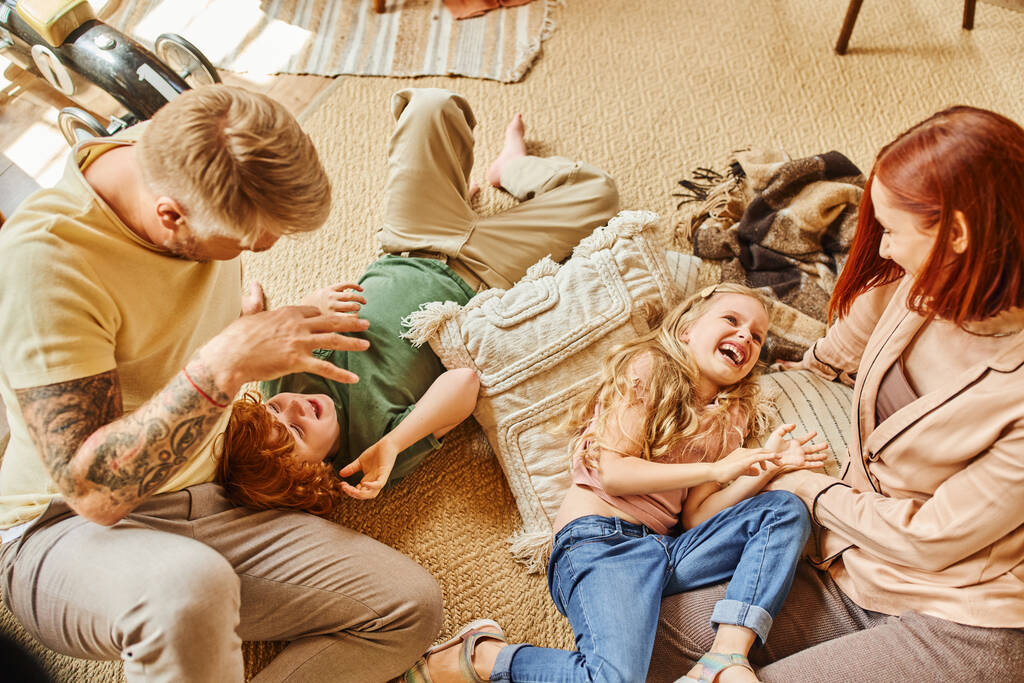 vista superior de los padres jugando con niños despreocupados en el suelo en la acogedora sala de estar en casa, momentos alegres - Foto, imagen