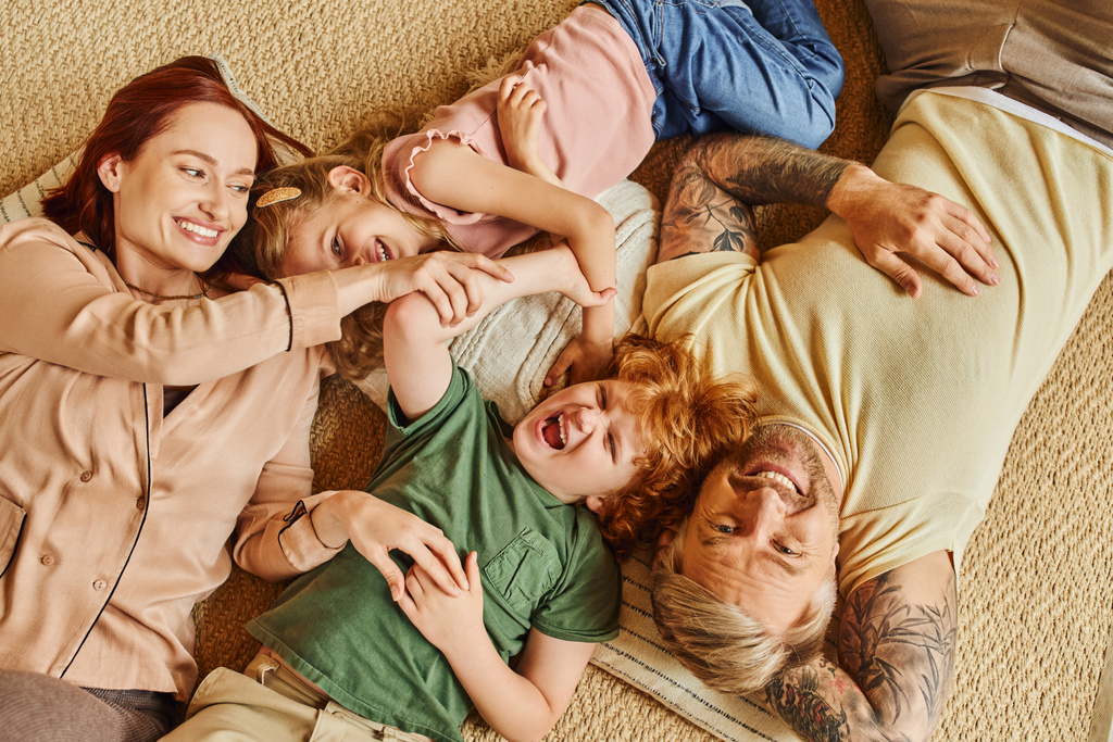 κορυφαία άποψη των ευτυχισμένων γονιών και των παιδιών ξαπλωμένοι και στο πάτωμα και γελώντας στο μοντέρνο σαλόνι - Φωτογραφία, εικόνα