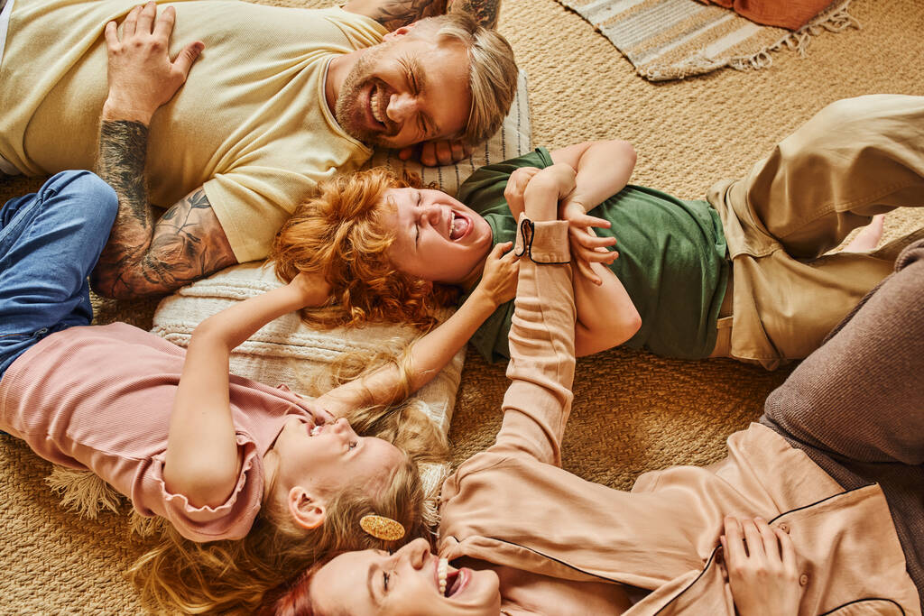 vista de alto ângulo de pais e crianças se divertindo no chão na sala de estar moderna, momentos acarinhados - Foto, Imagem
