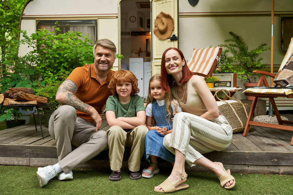 vrolijk ouders met gelukkige kinderen zitten in de buurt trailer huis en op zoek naar camera, familie vrije tijd - Foto, afbeelding