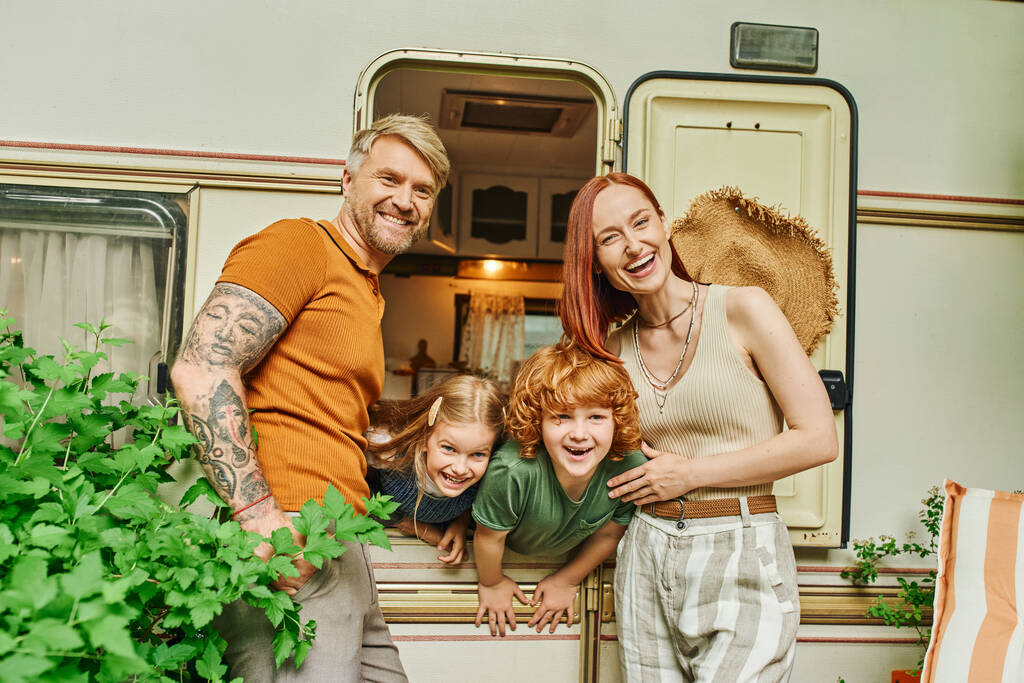 laughing couple looking at camera near kids having fun in trailer home, adventure and relaxation - Photo, Image