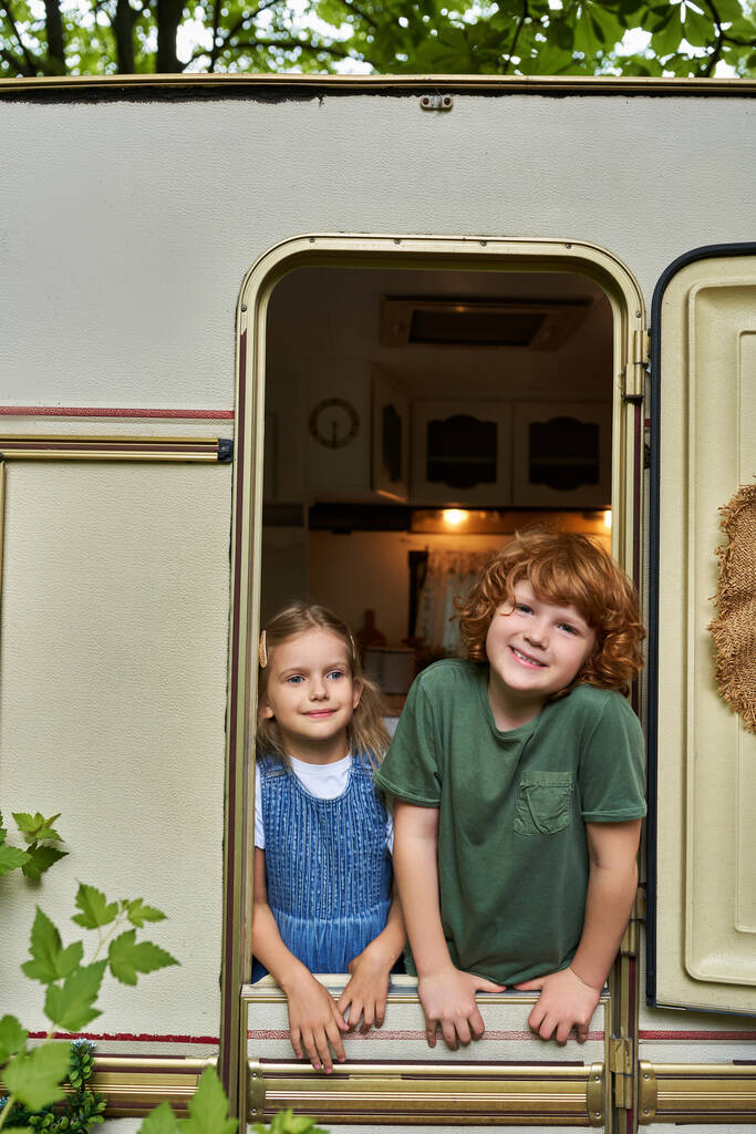 gelukkig roodharige jongen kijken naar camera van trailer huis in de buurt schattig zus, broers en zussen relatie - Foto, afbeelding