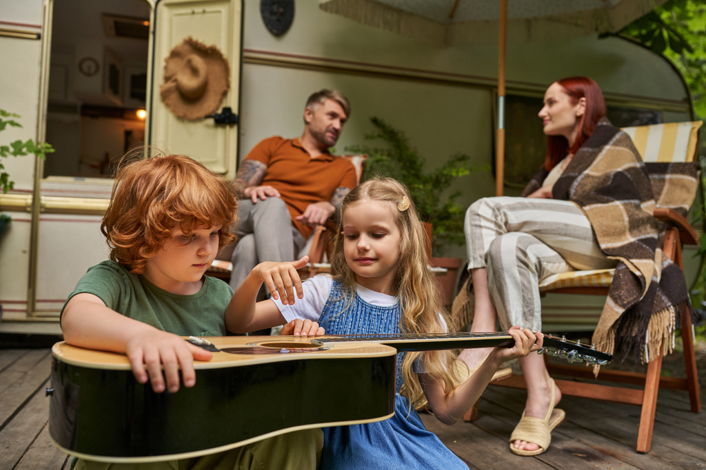 vörös hajú gyermek tanul gitározni közeli testvér és a szülők ül és beszél lakókocsi otthon - Fotó, kép
