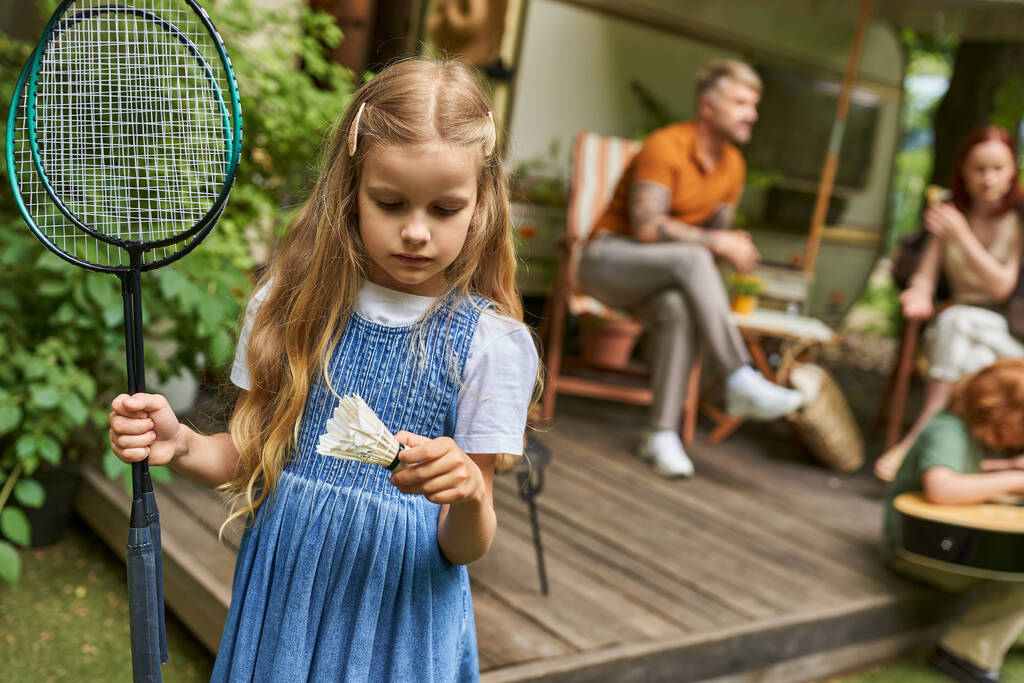 fille tenant roquettes de badminton et navette près de la famille et la maison de remorque sur fond flou - Photo, image