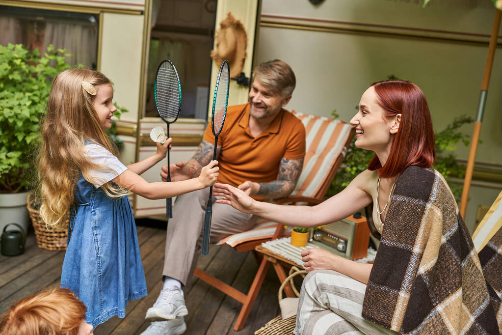 boldog lány ad tollaslabda rakéták és shuttlecock a szülők ül a modern lakókocsi otthon - Fotó, kép